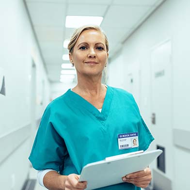 A smiling middle aged nursing student is seated at home, in front of her laptop, and actively participating in an online class.