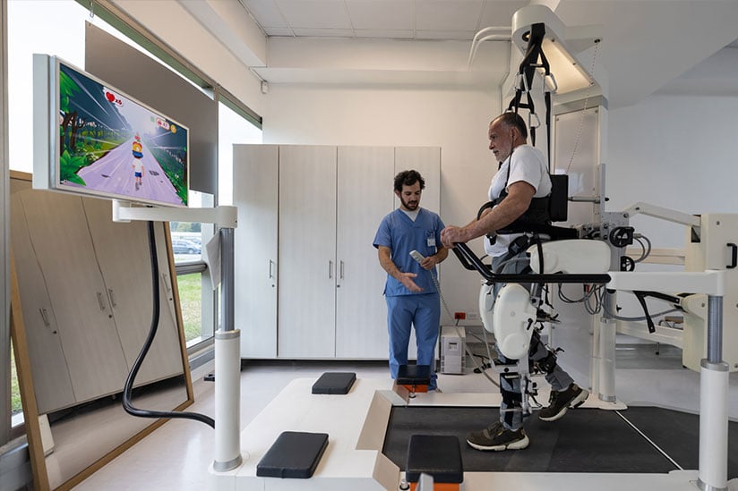 A nurse in blue scrubs assists a patient using a high-tech gait training machine with a virtual reality screen, showcasing the integration of advanced technology in nursing rehabilitation.